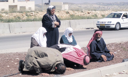 Friday, 2pm, Qalandiya. As a sermon is broadcast six Palestinians pray by the roadside.